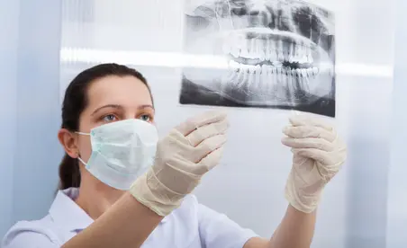 Eine Zahnärztin in Schutzkleidung betrachtet aufmerksam ein dental-radiografisches Bild.